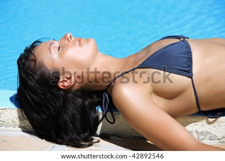 young beautiful caucasian brunette woman relaxing or sleeping near a swimming pool getting tanned by the su