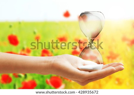 Hourglass in female hand on field of poppies background