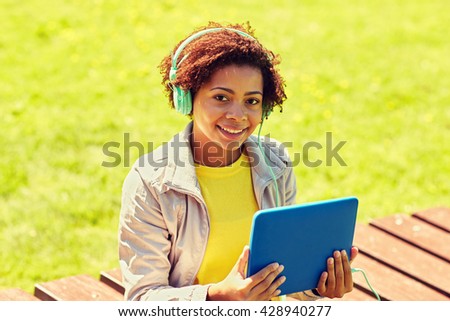 technology, lifestyle and people concept - smiling african american young woman or teenage girl with tablet pc computer and headphones listening to music in summer park