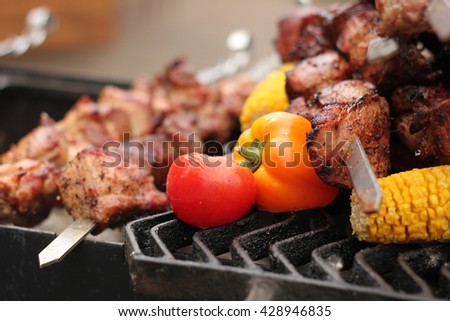 Skewers with meat of pork and chicken cooked on the grill on the grill. Also pictured eating vegetables. Tomatoes, peppers, corn.