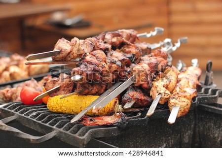 Skewers with meat of pork and chicken cooked on the grill on the grill. Also pictured eating vegetables. Tomatoes, peppers, corn.
