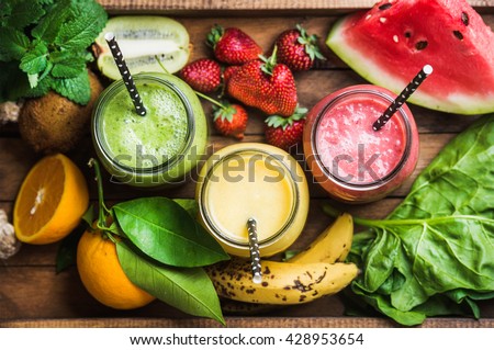 Freshly blended fruit smoothies of various colors and tastes in glass jars in rustic wooden tray. Yellow, red, green. Top view, selective focus Royalty-Free Stock Photo #428953654