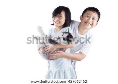 Picture of two cheerful children playing in the studio and smiling at the camera while holding a siberian husky puppy