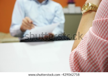 Close-up of business meeting, Two businessmen discussing a deal ,signing a contract on white table, with close up waiting person and the far blurred decision-makers person in the orange wall painted