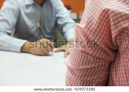 Close-up of business meeting, Two businessmen discussing a deal, signing a contract on white table, with close up waiting person and the far blurred decision-makers person in the orange wall painted