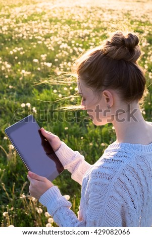 Girl standing and holding a tablet computer in the sunset light