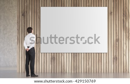 Businessman looking at large poster hanging on wooden plank wall in room with concrete floor. Mock up, 3D Rendering