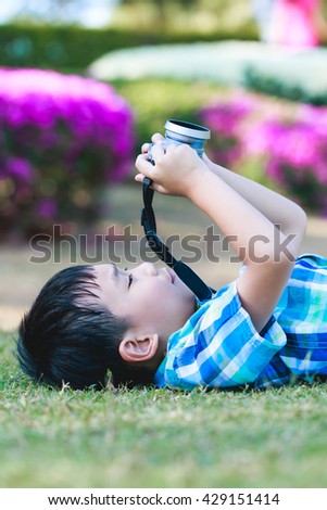 Handsome asian boy taking photo by vintage film camera, exploring nature at park, on summer in the day time. Child in nature, outdoors portrait. Active lifestyle, curiosity, pursuing a hobby concept.