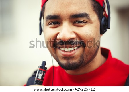 Cheerful black boy smoking electronic cigarette and listening to music
