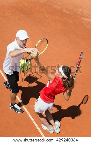 Junior tennis player in training with coach, practicing service