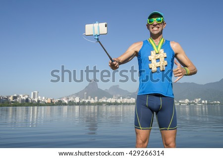 Hashtag gold medal athlete posing for a picture with his mobile phone on a selfie stick at Lagoa Rodrigo de Freitas Lagoon in Rio de Janeiro, Brazil
