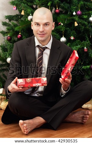 Bald smiling businessman opens a red gift under the tree