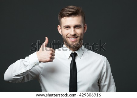 Everything is alright! Young handsome businessman showing thumbs up sign isolated on dark gray background.