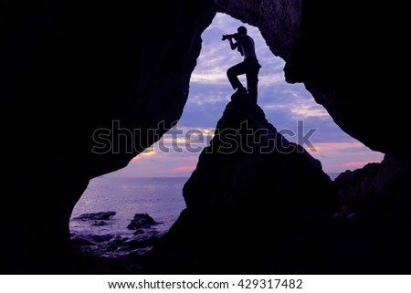 The man with camera stay in front of the cave near the sea with purple sky in the morning.
