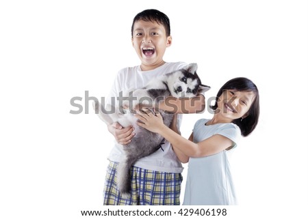 Picture of two excited children standing in the studio while holding a siberian husky puppy, isolated on white background