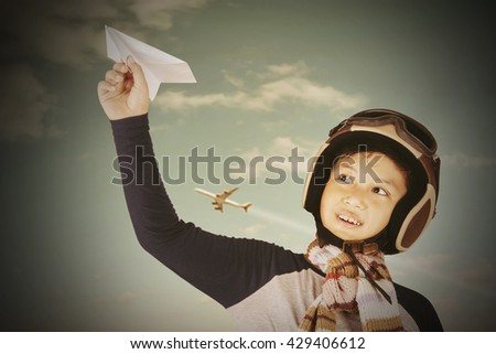 Picture of a male child playing a paper plane while wearing helmet outdoors