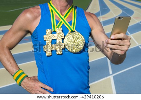 Hashtag gold medal athlete using his mobile phone standing outdoors on a blue and tan running track
