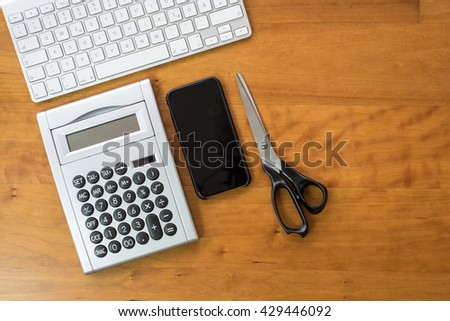 wooden desk with keyboard, smartphone, calculator and scissors