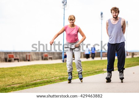 Active young people friends in training suit rollerskating outdoor. Woman and man riding enjoying sport.
