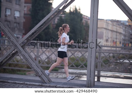 sporty woman running on sidewalk at early morning with city  sunrise scene in background