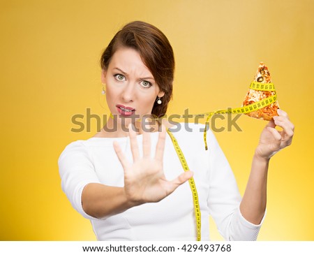 Closeup portrait serious woman saying no to fatty pizza with measuring tape around, trying to withstand, resist temptation to eat it isolated on yellow background. Human facial expression Royalty-Free Stock Photo #429493768