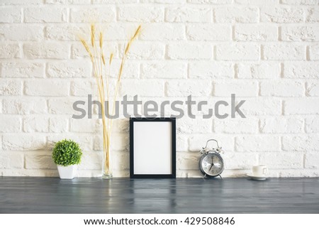 Blank picture frame, alarm clock, plant, wheat spikes and coffee cup on wooden desktop and white brick wall background. Mock 