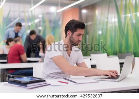 male student in classroom working  homework  and learning with laptop computer, students group in background
