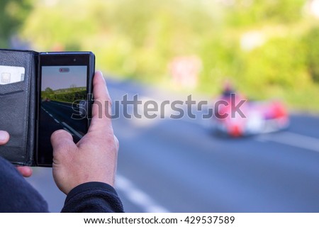 ISLE OF MAN, UK - MAY 31 2016: riders undertake qualifying laps of the annual TT (Tourist Trophy). Spectator taking photo with mobile phone. 