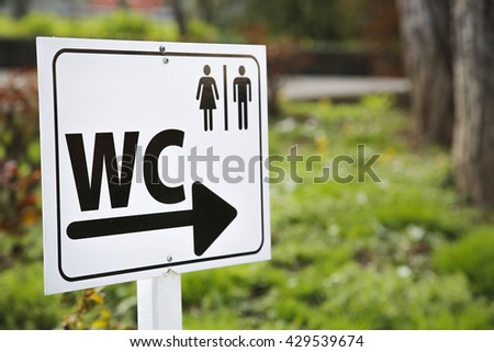 Toilet sign for man and female on white table outside in field