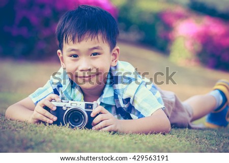 Asian boy taking photo by vintage film camera on blurred nature background at the day time. Concepts of creativity, strengthen the imagination of child. Vintage picture style.