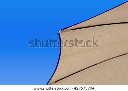 Grey fabric beach umbrella with blue edging on  blue sky background, close up, 
bottom view from the beach lounger