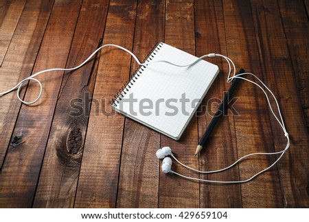 Blank sketchbook with a pencil and headphones on vintage wooden table background. Template for graphic designers portfolios.