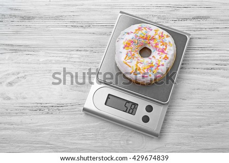 Donut with digital kitchen scales on wooden background