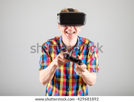 Young man playing with virtual reality glasses and video game controller isolated on a gray background