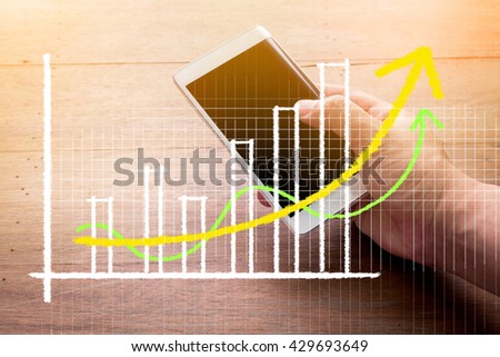 Close up of a man using mobile smart phonewith business graph with wooden background.jpg