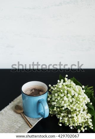 A cup of hot coffee and a bouquet of fragrant lilies of the valley.