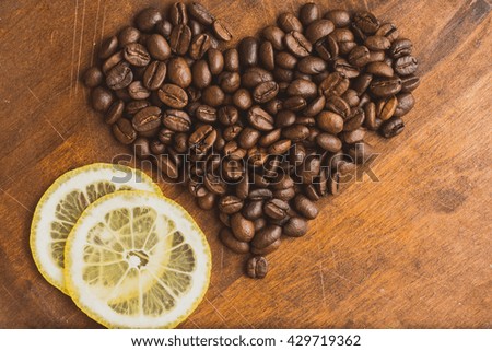 Brown coffee beans in shape of heart with lemon, closeup of macro coffee beans for background and texture. On brown wooden board.