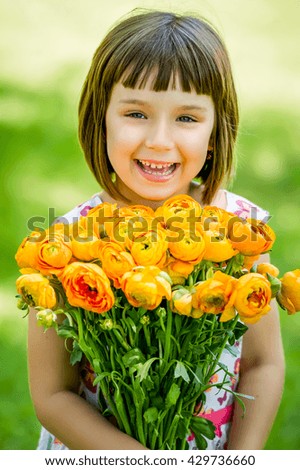 Beautiful little girl with a bouquet of flowers in arms, happy girl laughing to the photo camera   