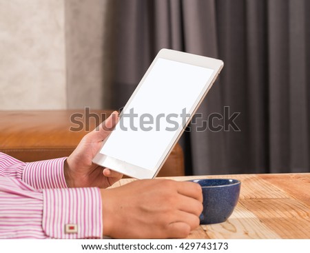 hands of a man holding blank tablet device over a wooden workspace table
