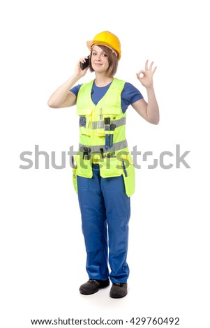 smiling construction female worker in yellow helmet and reflective vest speaking on mobile phone and showing okay sign isolated on white background. proposing service. advertisement gesture