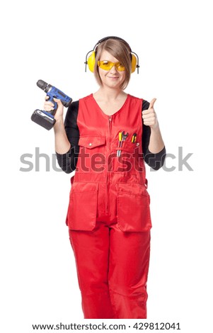portrait of smiling construction female worker holding a drill and showing thumb up isolated on white background
