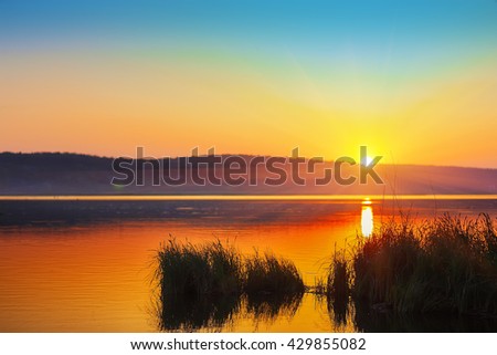 Beautiful sunset over calm lake. Dusk time. reeds at foreground