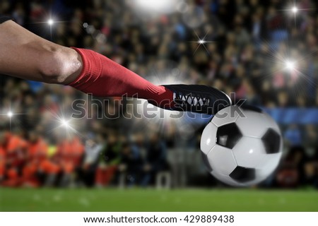close up leg and soccer shoe of football player in action kicking ball wearing red jersey and sock playing on stadium with audience flashes  and lens flare on the background 