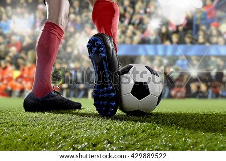close up legs and feet of football player in action wearing blue socks and black shoes running and dribbling with the ball playing match on green grass pitch at  soccer stadium with flashes and flare