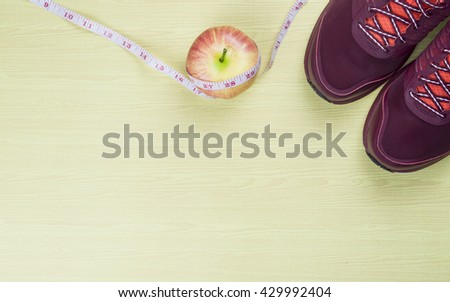 Sport shoes and apple wrapped in measuring tape on wooden background. Top view sport equipment. Selective focus.