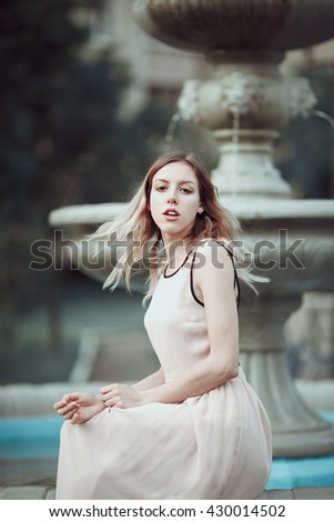 Beautiful young girl in fashionable pink dress standing near vintage stone fountain.Fairytale. Fashion. Fantasy