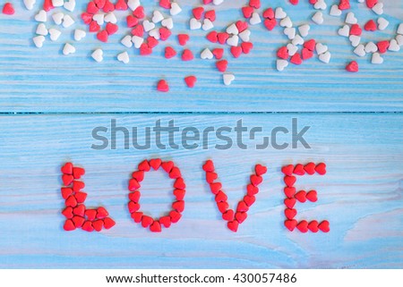 Red candy hearts laying on light blue painted rustic wooden background. Word LOVE made from candy hearts.