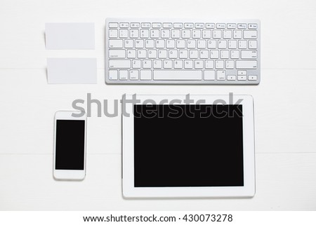 Keyboard with tablet, phone, business card on wooden table, top view