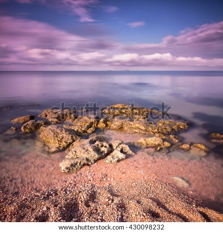 Seascape with rocks and sand in the foreground with two ships on the horizon. Long exposure