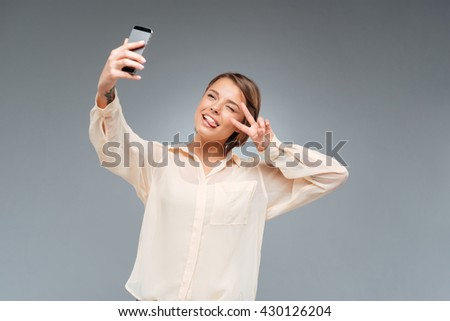 Young beautiful girl taking selfie and making victory sign over white background